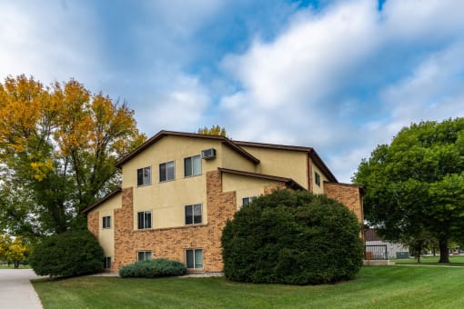 The view of an apartment building with green grass and trees. Fargo, ND Huntington Apartments.