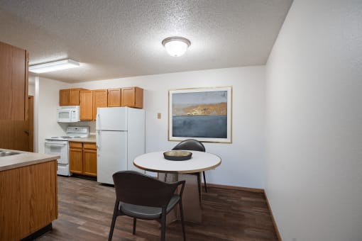 a kitchen and dining area with a table and chairs and a refrigerator. Fargo, ND Prairie Park Apartments