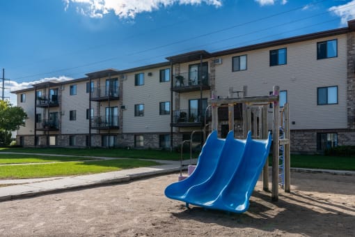 Fargo, ND Prairie Park Apartments. A playground with two blue slides in front of an apartment building