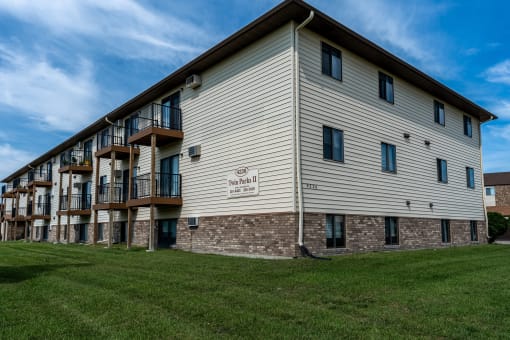 The exterior of a three level apartment building with a grass area out front