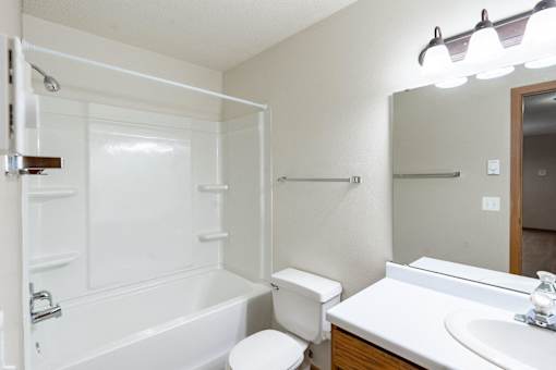 a bathroom with a shower toilet and sink and a mirror. Fargo, ND Briar Pointe Apartments
