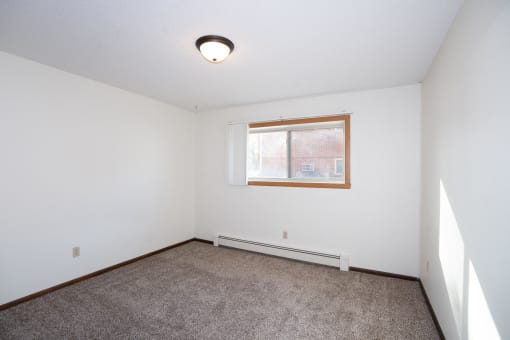 an empty room with carpet and a window. Fargo, ND Country Club Apartments