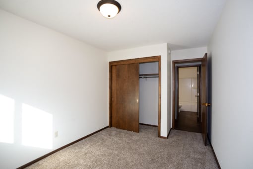 a room with a carpeted floor and a door to a closet and a hallway. Fargo, ND Country Club Apartments