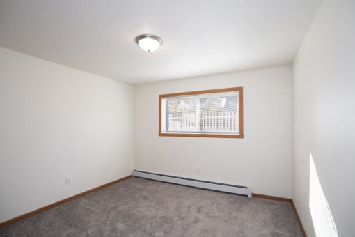 an empty living room with carpet and a window. Fargo, ND Country Club Apartments
