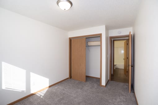 an empty living room with a door to a closet and a hallway to a bathroom. Fargo, ND Country Club Apartments