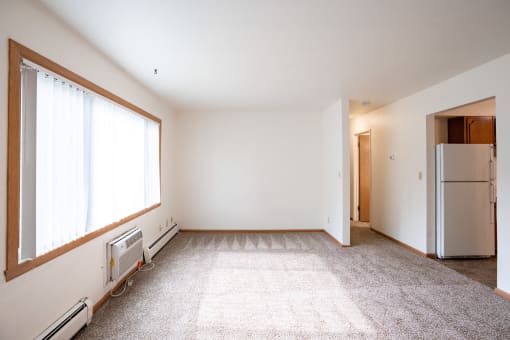 an empty living room with a large window and a refrigerator. Fargo, ND Crown Court 1 Apartments