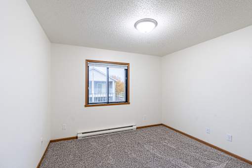an empty living room with carpet and a window. Fargo, ND Flagstone Apartments