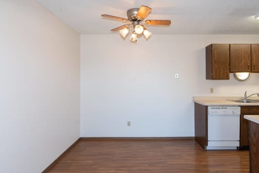 an empty living room with a ceiling fan and a kitchen. Fargo, ND Hartford Apartments