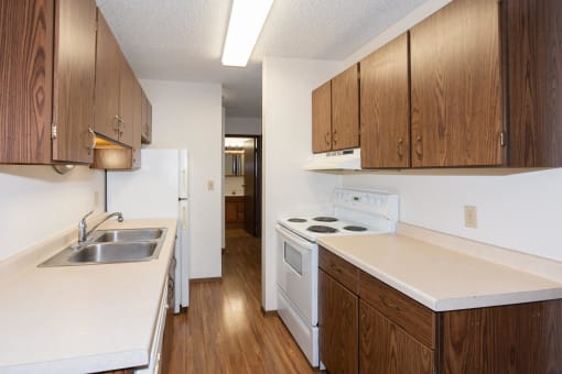 an empty kitchen with white appliances and wooden cabinets. Fargo, ND Hartford Apartments
