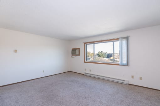 an empty living room with a large window and carpet. Fargo, ND Hartford Apartments