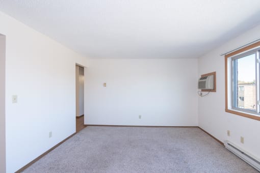 the living room of an apartment with carpet and a window. Fargo, ND Hartford Apartments