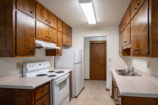 an empty kitchen with white appliances and wooden cabinets. Fargo, ND Hawn Apartments