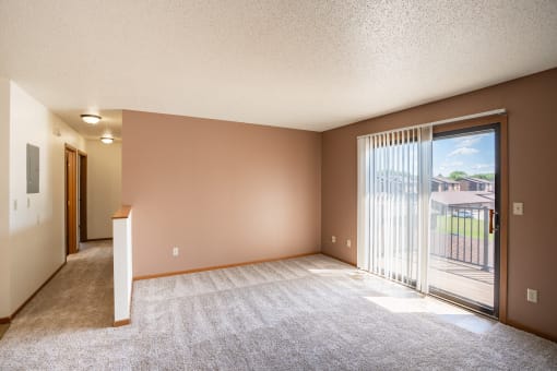 an empty living room with a sliding glass door to a balcony. Fargo, ND Hunters Run 2 Apartments
