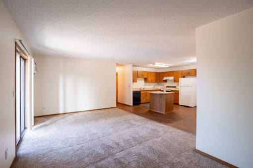 an empty living room with a kitchen with white appliances. Fargo, ND Kentwood Manor Apartments