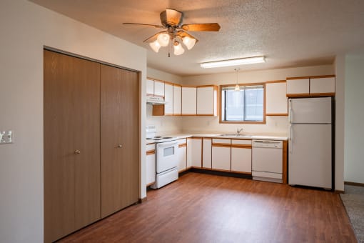 an empty kitchen with white appliances and wooden floors and a ceiling fan. West Fargo, ND Lake Crest Apartments 21e