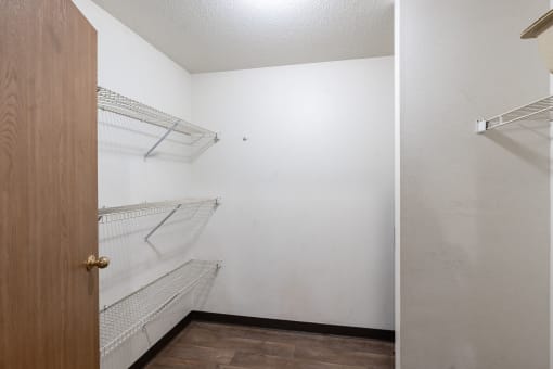 an empty closet with white walls and shelves and a wooden door. Fargo, ND Oxford Apartments