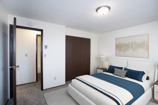 a bedroom with a blue and white bed and a closet. Fargo, ND Pacific Park Apartments