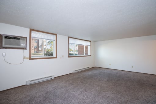 the living room of an apartment with carpet and a window. Fargo, ND Pacific Park Apartments