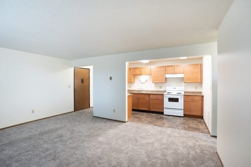 an empty living room with a kitchen with wood cabinets