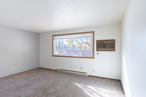 an empty living room with carpet and a window. Fargo, ND Pacific Park Apartments