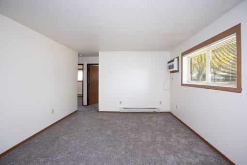 an empty living room with a large window and white walls. Fargo, ND Pacific South Apartments