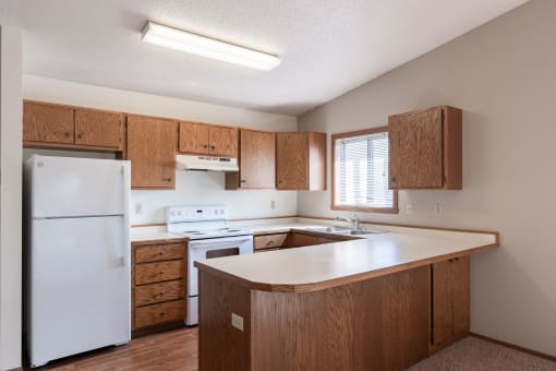 an empty kitchen with white appliances and wooden cabinets. Fargo, ND Rosegate Apartments