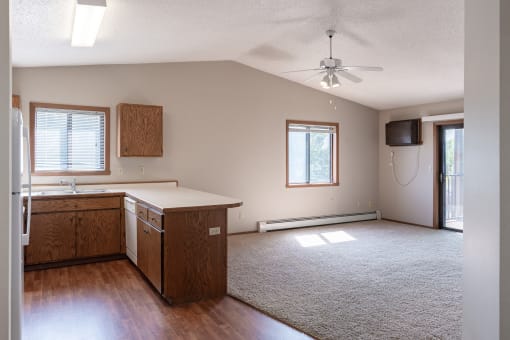 an empty living room with a kitchen and a ceiling fan. Fargo, ND Rosegate Apartments