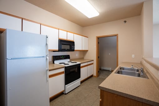a kitchen with white appliances and a sink and a refrigerator. West Fargo, ND West Lake Apartments 11A