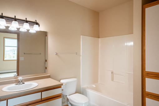 the view of a bathroom with a toilet sink and tub and a mirror. West Fargo, ND West Lake Apartments 11A
