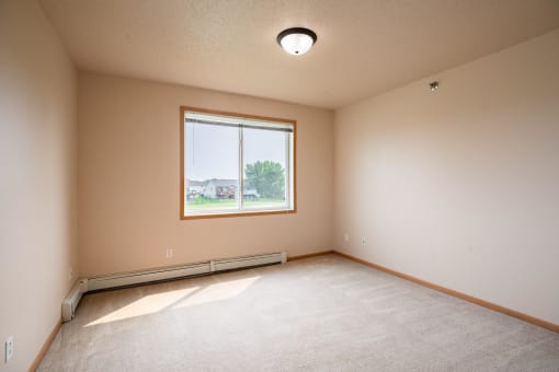 the spacious living room has a large window and beige carpet
