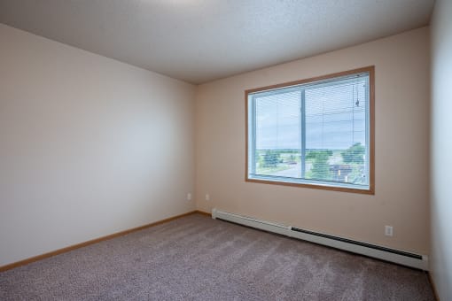 an empty bedroom with a large window and carpeting. Fargo, ND West Lake Apartments