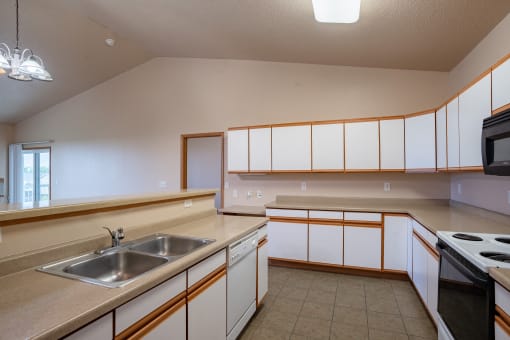 a kitchen with white cabinets and a living room in the background. Fargo, ND West Lake Apartments