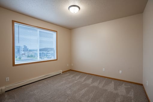 a bedroom with a large window and carpeted floors. Fargo, ND West Lake Apartments