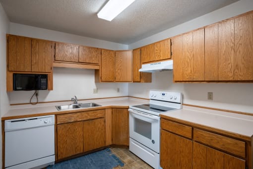 an empty kitchen with white appliances and wooden cabinets. Fargo, ND Westview Towers Apartments