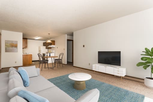 Grand Forks, ND Autumn Apartments. a living room with a white couch and a blue rug and a kitchen and diing room in the background.