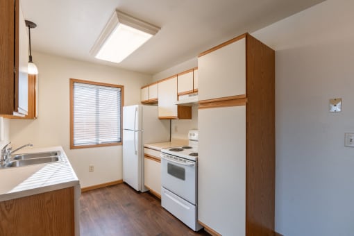 a kitchen with white appliances and wooden cabinets and a window. Grand Forks, ND Autumn Ridge Apartments