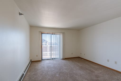 an empty living room with a sliding glass door to a balcony. Grand Forks, ND Autumn Ridge Apartments