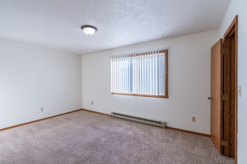 a bedroom with carpet and a window. Grand Forks, ND Cedarwood Apartments
