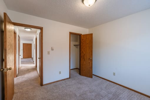 a bedroom with a carpeted floor and a hallway with two doors and a closet. Grand Forks, ND Cedarwood Apartments