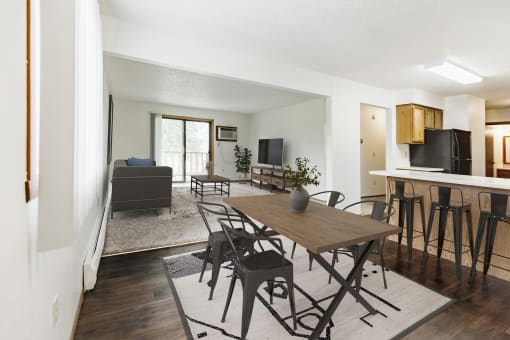 Grand Forks, Chandler 1802 Apartments. An dining room with a dining table and chairs and a living room with a couch and tv in the background