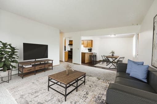 Grand Forks, Chandler 1802 Apartments.  A living room with a couch a coffee table and a tv and a dining room and kitchen in the background