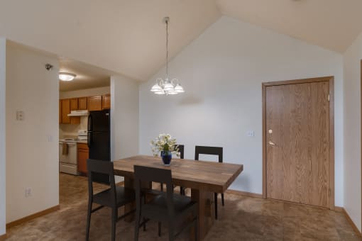 A dining room and kitchen with a wooden table and chairs. Grand Forks, ND Creekside Apartments.