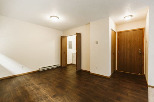 Grand Forks Harrison Apartments. A living room of an empty apartment with wood flooring and a wooden door