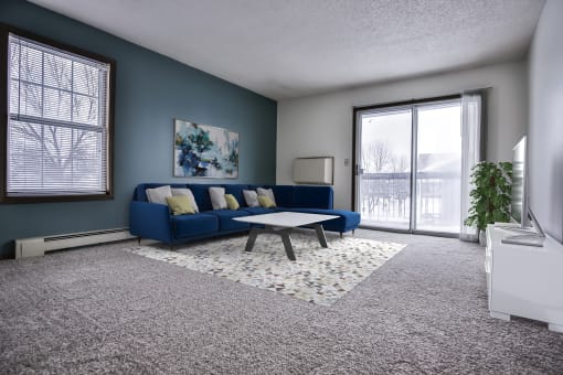 Grand Forks Primrose Apartment.  A living room with a blue couch and coffee table in front of a sliding glass door