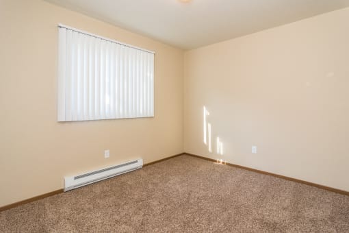 Grand Forks, ND Stanford Court Apartments. A kitchen with black appliances and a living room in the background a bedroom with a large window and a carpeted floor