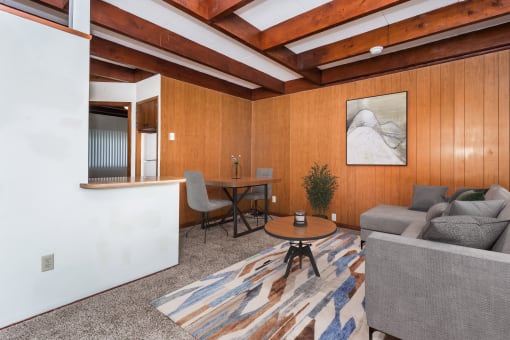 Grand Forks, ND Washington Apartments a living room with wood paneling and a beamed ceiling with a couch and dining area in the background