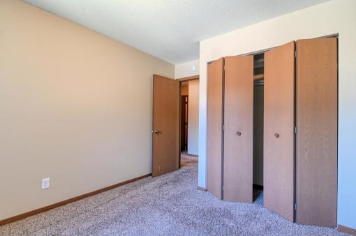 Grand Forks, ND Madison Apartments. A bedroom with a closet and carpeted floors.