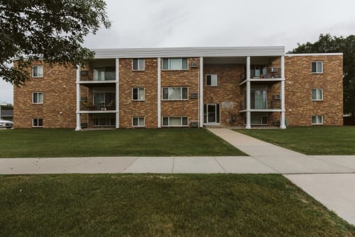 Grand Forks, ND Hoven Lane Apartments. an exterior view of a brick apartment building with grass and a sidewalk