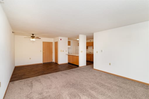 an empty living room with a ceiling fan and a kitchen. Hutchinson, MN Deer Park Apartments