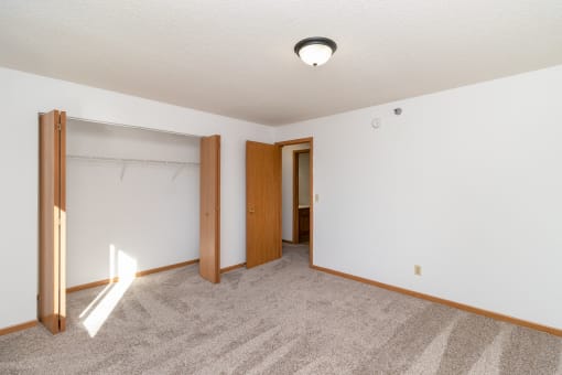 an empty living room with carpet and a door to a closet. Hutchinson, MN Deer Park Apartments